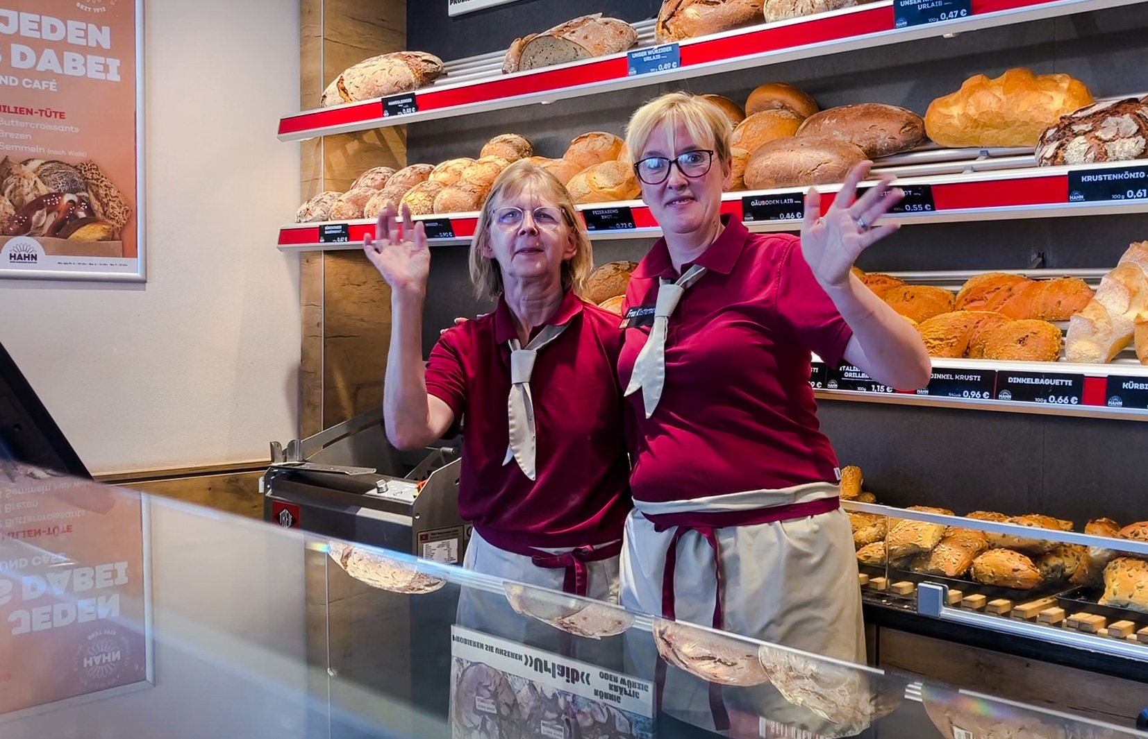 Zwei Verkäuferinnen stehend winkend vor Theke einer Bäckerei