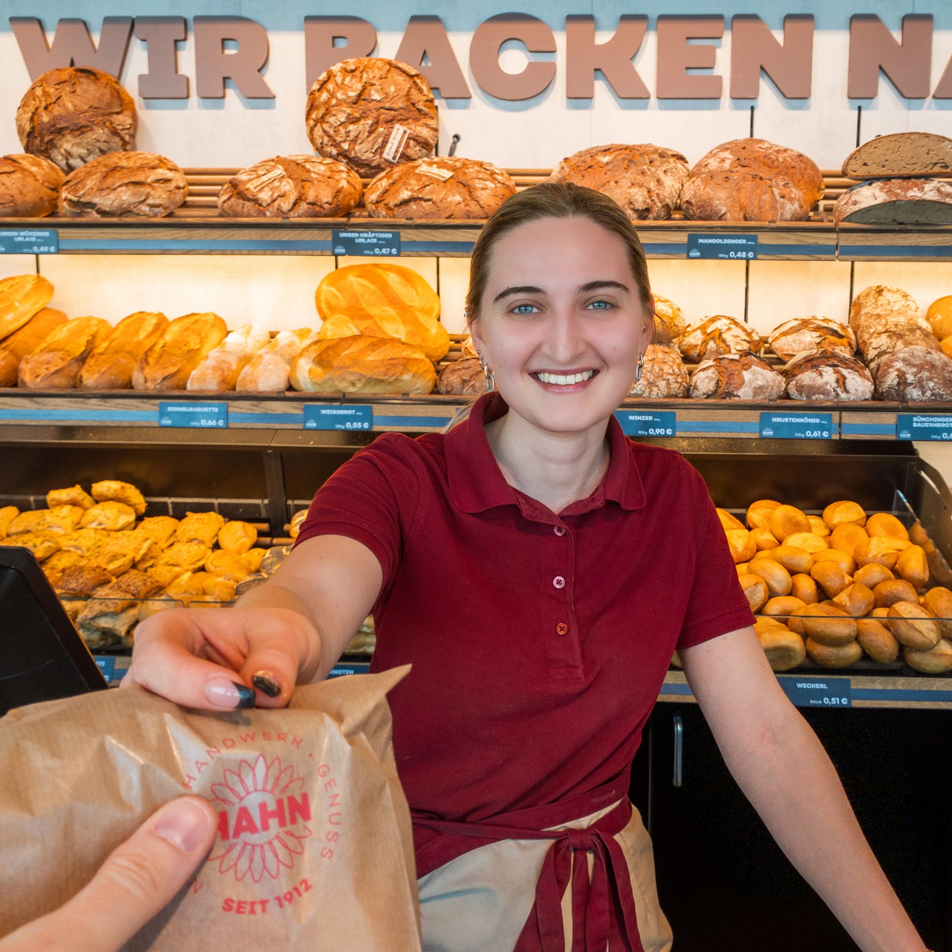 Bäckereiverkäuferin reicht einem Kunden eine Tüte über die Theke