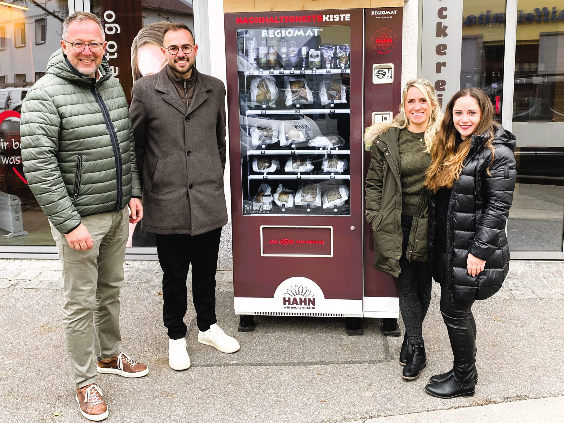 Vier Personen stehen vor einem Verkaufsautomaten der Bäckerei Hahn